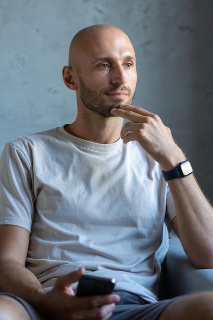 A young successful stylish man with a cleanshaven head Portrait of a businessman sitting in a chair with a smartphone in his hand