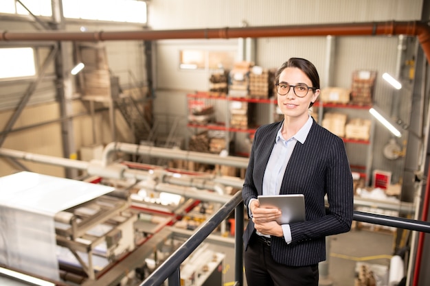 Young successful technical manager in formalwear looking at you while working in warehouse of industrial plant