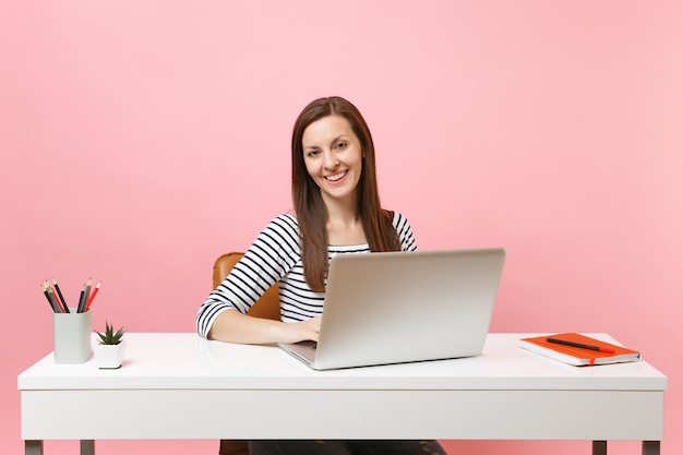 Young successful woman in casual clothes working on project with laptop while sitting at office 