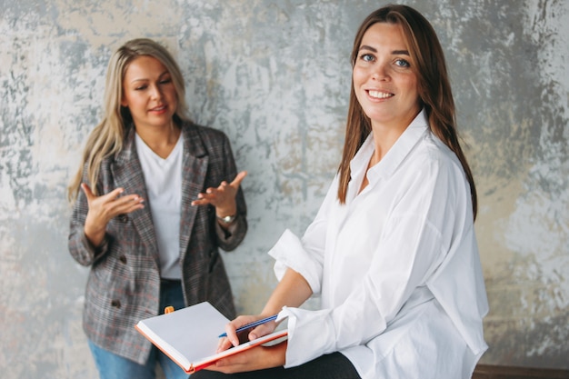 Young successful women colleagues discuss joint project, coaching or mentoring in modern loft office