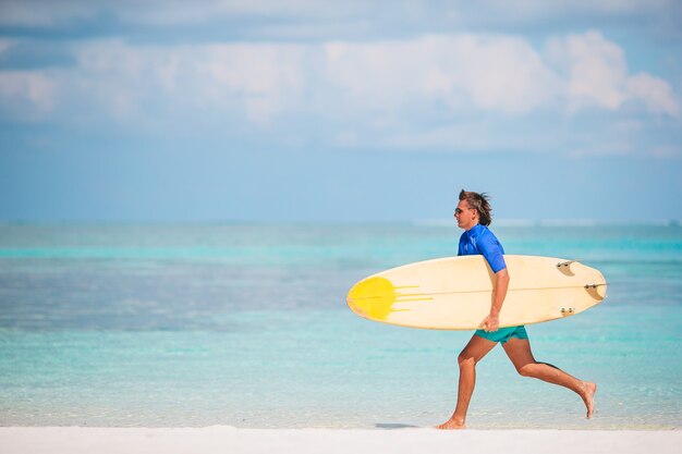 Young surf man at white beach with yellow surfboard