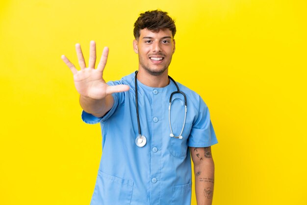 Young surgeon doctor man isolated on yellow background counting five with fingers