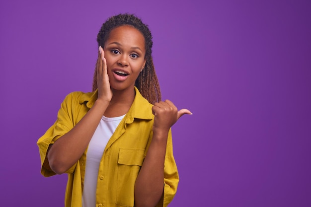 Young surprised african american woman pointing with finger at copy space