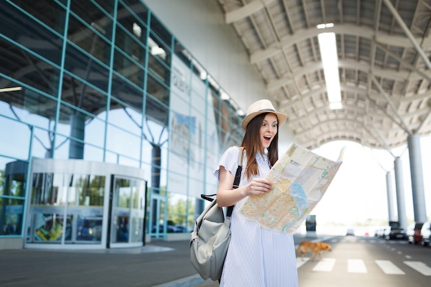 Young surprised traveler tourist woman with backpack holding paper map at international airport