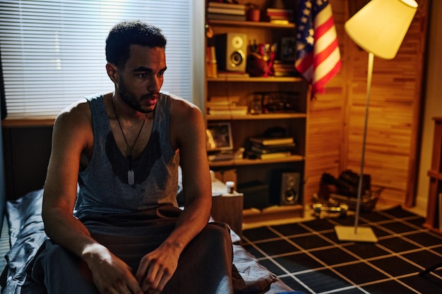 Young sweaty man in vest sitting on bed in the middle of the night