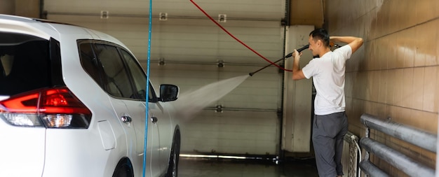 Young tall man spalshing his car by garden hose