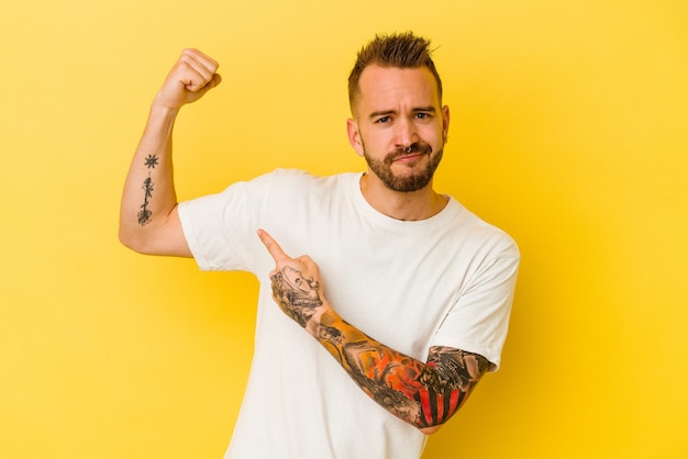 Photo young tattooed caucasian man isolated on yellow background showing strength gesture with arms, symbol of feminine power