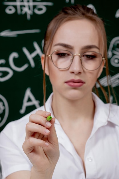 Young teacher is sitting near blackboard in classroom