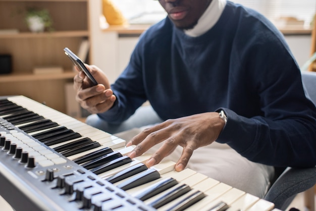 Young teacher of music with smartphone touching keys of piano keyboard