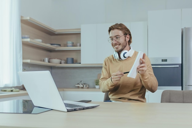 Young teacher teaches remotely from home man works in kitchen at home uses laptop for online call