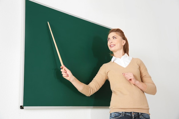 Young teacher with pointer beside blackboard on white background