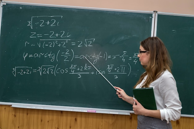 Young teacher writing and explain the mathematical formulas on a chalkboard.  Education