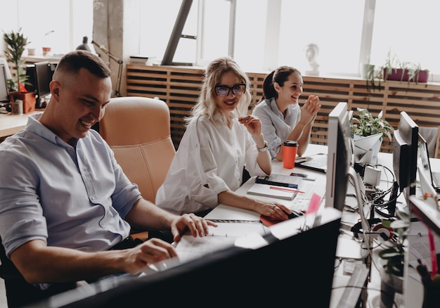 Young team of the colleagues works sitting at the desks with a laptop and documents in a light modern office