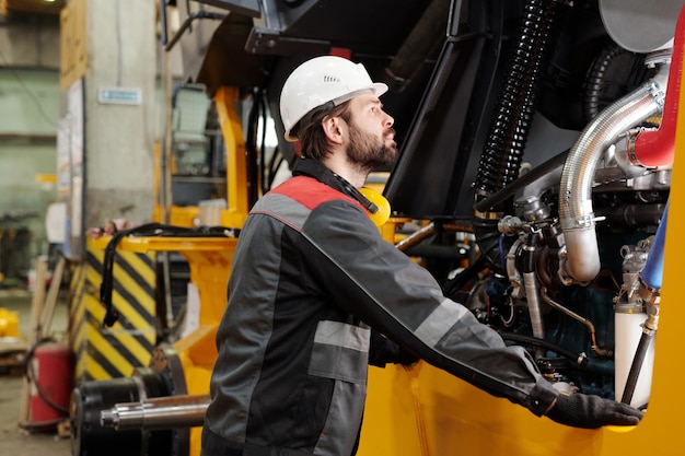 Young technician or repairman in hardhat standing by industrial machine