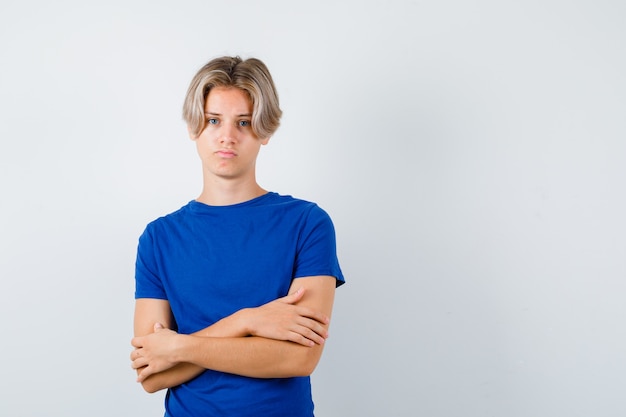 Young teen boy in blue t-shirt holding arms folded and looking displeased , front view.