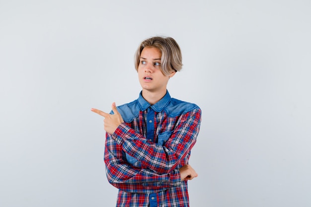 Young teen boy in checked shirt pointing left, looking aside and looking focused , front view.