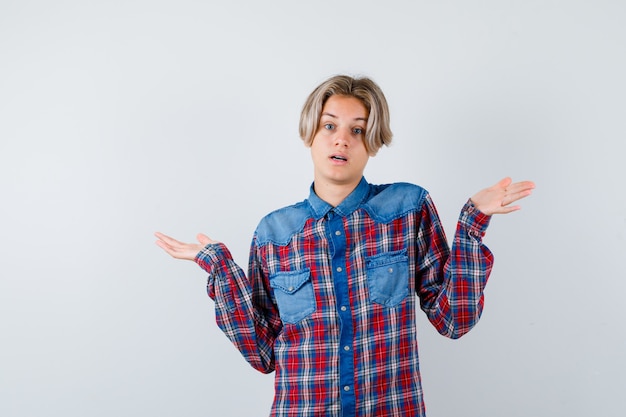 Young teen boy in checked shirt showing helpless gesture and looking bewildered