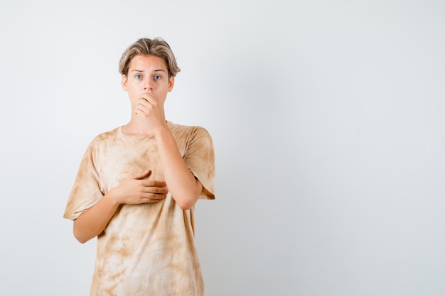 Young teen boy keeping hand on mouth in t-shirt and looking agitated. front view.