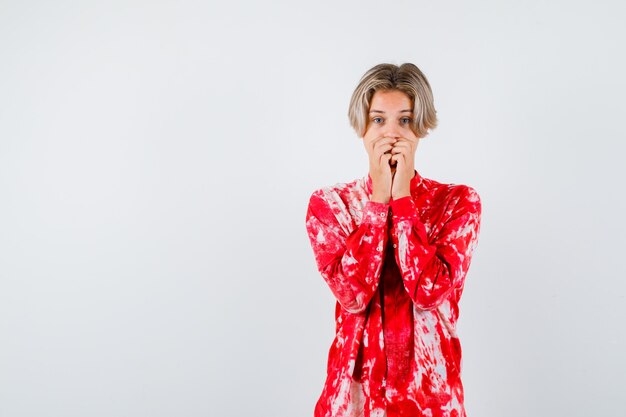 Young teen boy keeping hands on mouth in shirt and looking excited