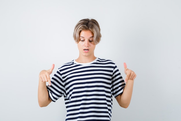 Young teen boy pointing down in striped t-shirt and looking focused. front view.