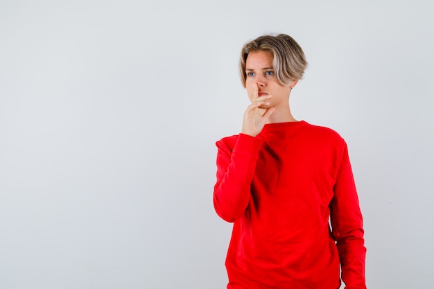 Young teen boy showing silence gesture in red sweater and looking serious , front view.