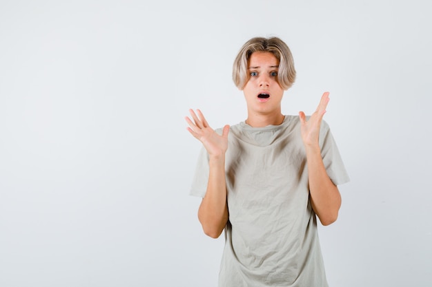 Young teen boy showing surrender gesture in t-shirt and looking frightened , front view.