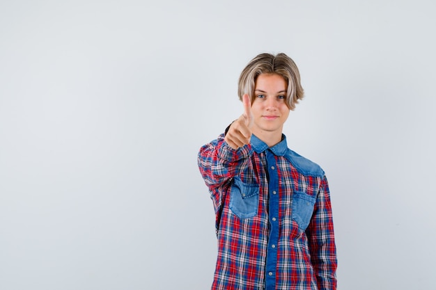 Young teen boy showing thumb up in checked shirt and looking proud , front view.