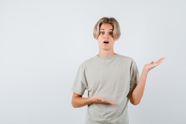 Young teen boy showing welcoming gesture in t-shirt and looking wondered. front view.