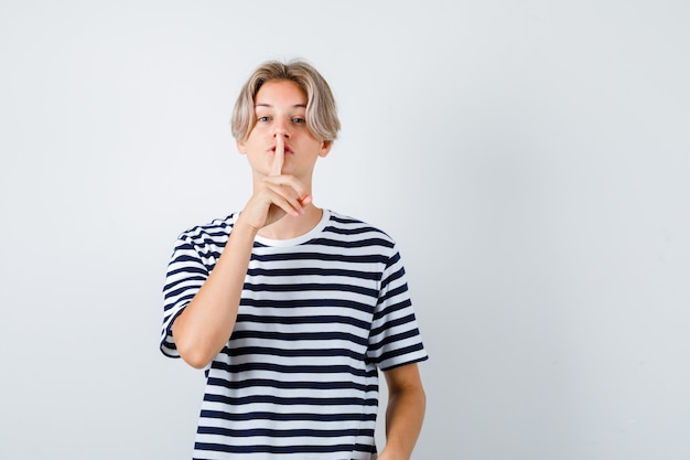 Young teen boy in striped t-shirt showing silence gesture and looking confident , front view.