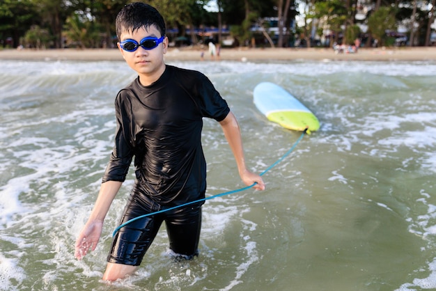 Young teen boy surfer holding rope of soft board bring it to try again in wave Rookie teenager surfboard student playing on water in strive focus action