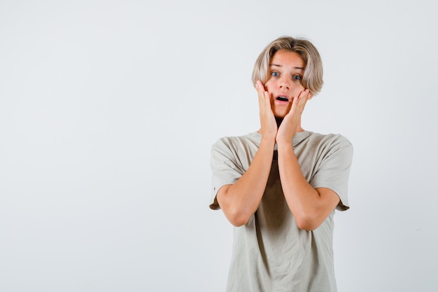 Young teen boy in t-shirt keeping hands on cheeks and looking anxious