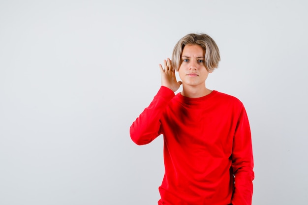 Young teen boy with hand near ear in red sweater and looking confused. front view.