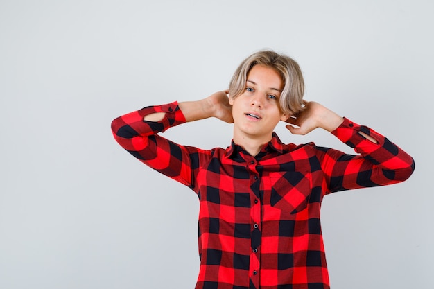 Young teen boy with hands behind head in checked shirt and looking relaxed , front view.