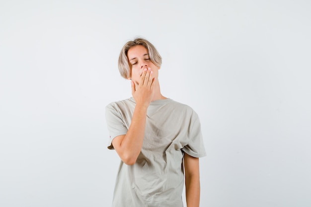 Young teen boy yawning in t-shirt and looking sleepy. front view.