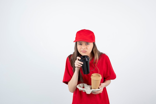 young teen girl in red uniform holding two cups of coffee in a carton