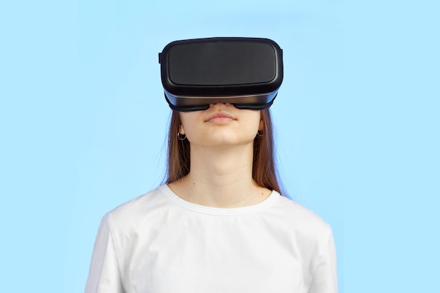 Young teen girl in a virtual reality helmet isolated on a blue background plays a 3d computer game.