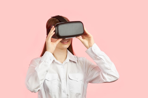 Young teen girl in a virtual reality helmet isolated on a pink background plays a 3d computer game.