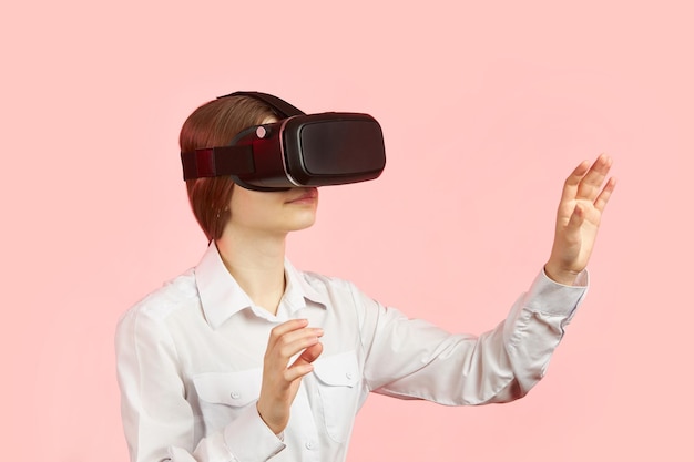 Young teen girl in a virtual reality helmet isolated on a pink background plays a 3d computer game.