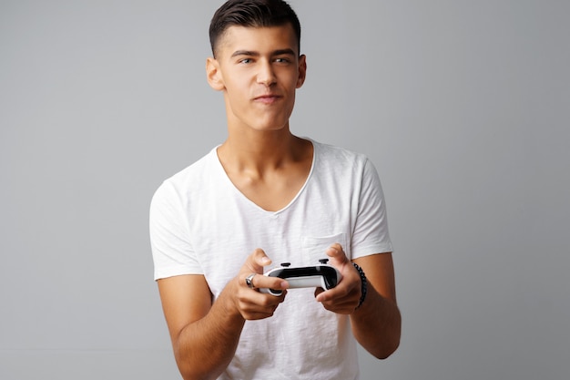 Young teen man playing with console joystick over a gray background