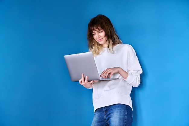 Young teenage female with laptop on blue background