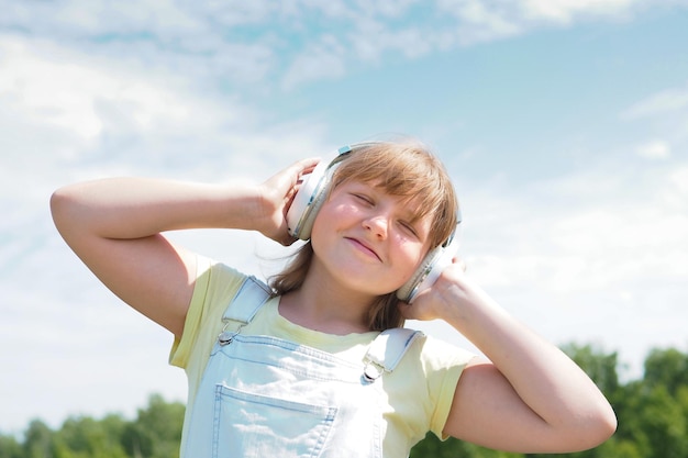 Young teenage girl walks in the park with headphones and smiles.