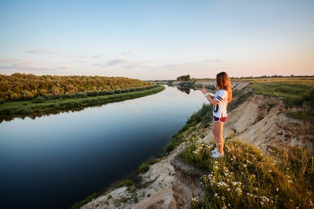 Photo young teenage girl in white t-shirt, violet shirts and white sneakers standing on the edge of the cliff of the river