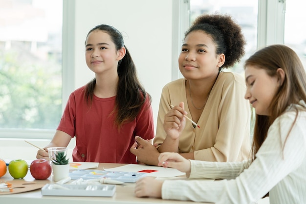 Young teenage woman listening teacher explain drawing and painting with watercolors at art school