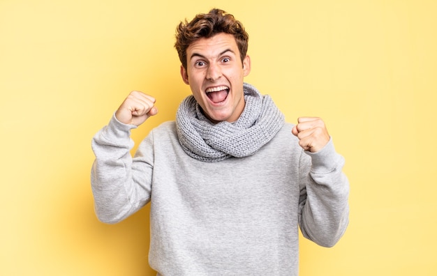 Young teenager boy feeling happy, surprised and proud, shouting and celebrating success with a big smile