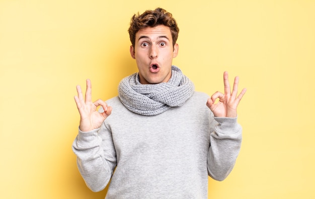 Young teenager boy feeling shocked, amazed and surprised, showing approval making okay sign with both hands