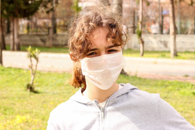 Young teenager girl with a medical mask in a park on a bench. Quarantine and isolation during coronavirus