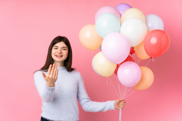 Young teenager holding lots of balloons inviting to come