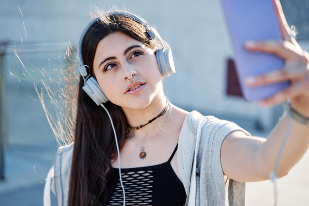 Young teenager taking a selfie with a mobile phone woman with headphones making a video call in the city