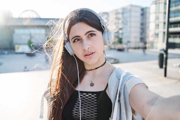 Young teenager taking a selfie with a mobile phone woman with headphones making a video call in the city