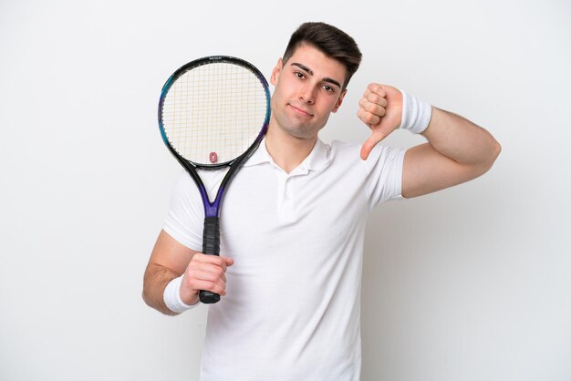 Young tennis player man isolated on white background showing thumb down with negative expression